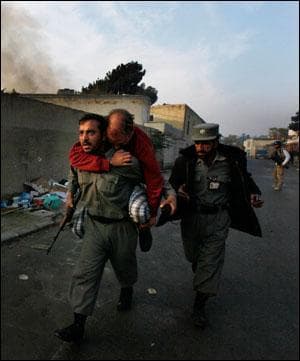 An Afghan police officer carries an injured unidentified German national as smoke bellows from the site of the attack in Kabul. (Gemunu Amarasinghe/AP)