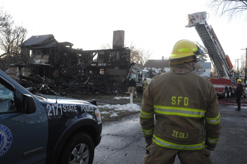 A firefighter stands in front of the remains of a house on 17 Fair St. in Northampton, Mass. on Sunday, Dec. 27. A father and son died in the house fire early Sunday morning as firefighters struggled to put out more than a half dozen blazes, authorities said. (AP)