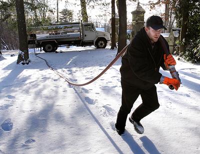 In this 2010 photo, Jason Kilpatrick of Wholesale Fuel hauled a hose across a snow-covered yard while delivering home heating oil in Framingham. (AP)
