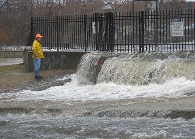 An official surveys flooding of the Charles River by the Moody Street dam in Waltham on Monday. (Jack Lepiarz for WBUR)