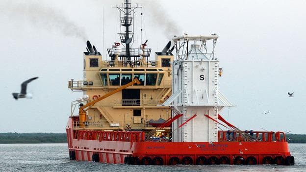 The barge Joe Griffin sails down a channel on its way to the Gulf of Mexico carrying the 100-ton concrete-and-steel containment chamber that will be used to help contain oil leaking from a blown-out wellhead. (AP)