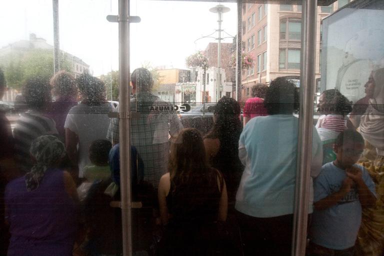 While waiting, riders crowd a bus stop in Cambridge's Central Square to avoid the rain. (Jess Bidgood for WBUR)