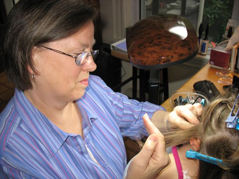 Helen Hadley methodically checks a 7-year-old girl’s head for live lice and eggs. A complete “comb through” can take several hours at a cost of $100 per hour. (Monica Brady-Myerov/WBUR)