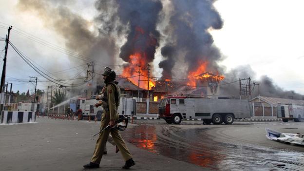 A policeman patrols as flames rise from a government building set on fire by protesters over the weekend in Srinagar, in Indian-administered Kashmir. (AP)