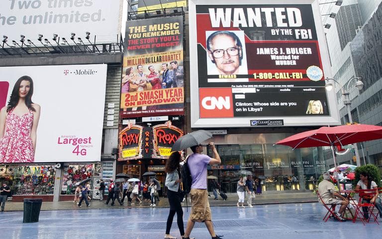 A couple walks past an FBI video looking for mob boss James "Whitey" Bulger on display in New York's Times Square,  Thursday, June 23, 2011. (AP)