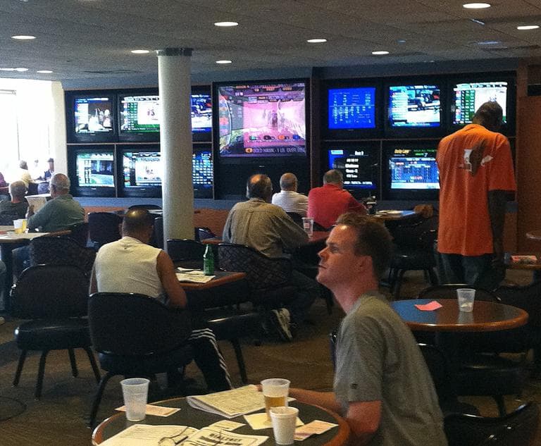 About 100 or so people watch muted TV screens in the clubhouse of Raynham Park. (Steve Brown/WBUR)