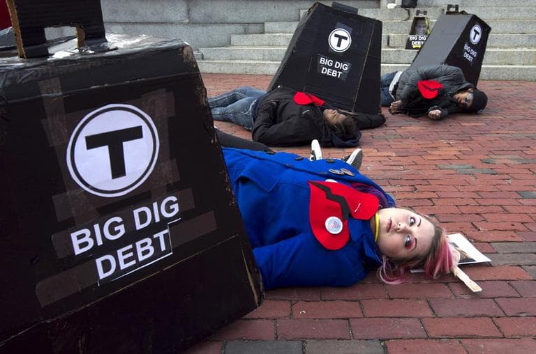 Protesters pretend to be crushed under an effigy of MBTA and so-called Big Dig debt along in front of the Statehouse in February. (AP)