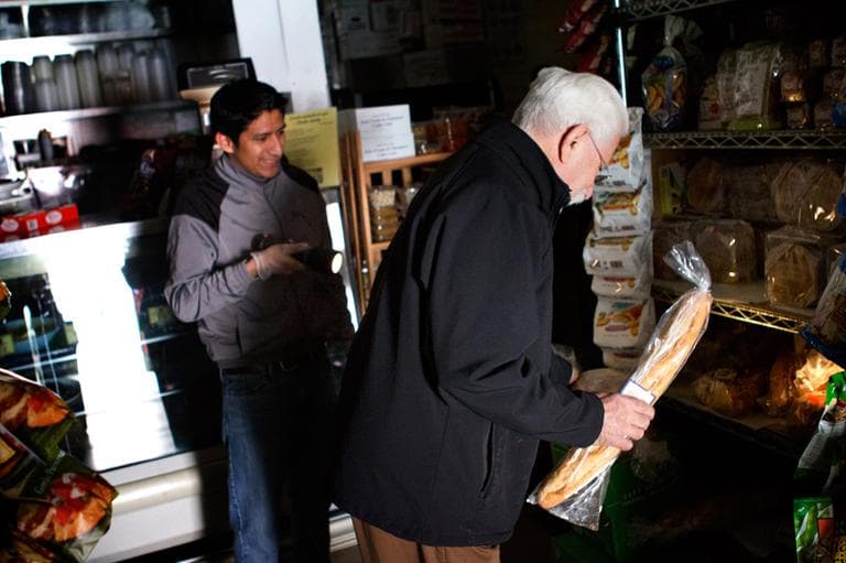 An employee of Deluca's Market on Newbury street helps a customer find what he is looking for with a flashlight. (Jesse Costa/WBUR)
