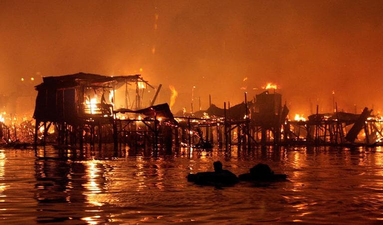 A man floats in the water with some of his belongings as his neighborhood is engulfed in fire Friday, May 11, 2012 in a slum area in Manila, Philippines. Officials say the fire that swept through a sprawling squatters' colony on Manila Bay's rim has left two people missing and some 10,000 others homeless. (AP Photo/Pat Roque)