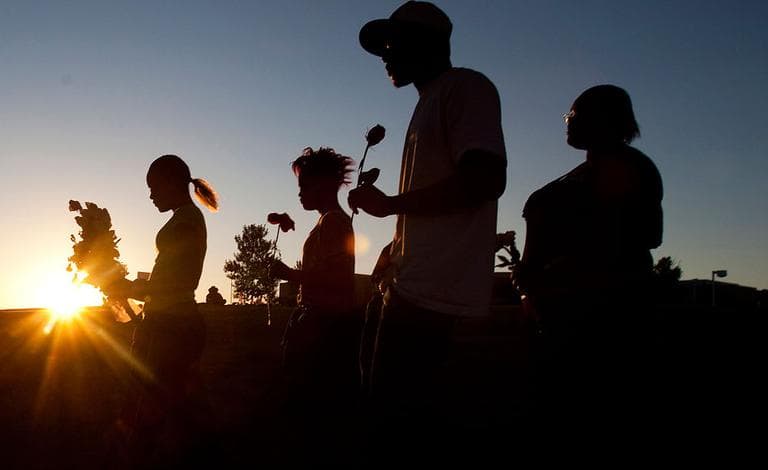 People carry flowers to lay at a makeshift memorial across the street from the Century Theater parking lot, in Aurora, Colo. July 21, 2012. Twelve people were killed when a gunman entered an Aurora, Colo., movie theater, released a canister of gas and then opened fire during opening night of the Batman movie "The Dark Knight Rises." (AP Photo/Barry Gutierrez, File)