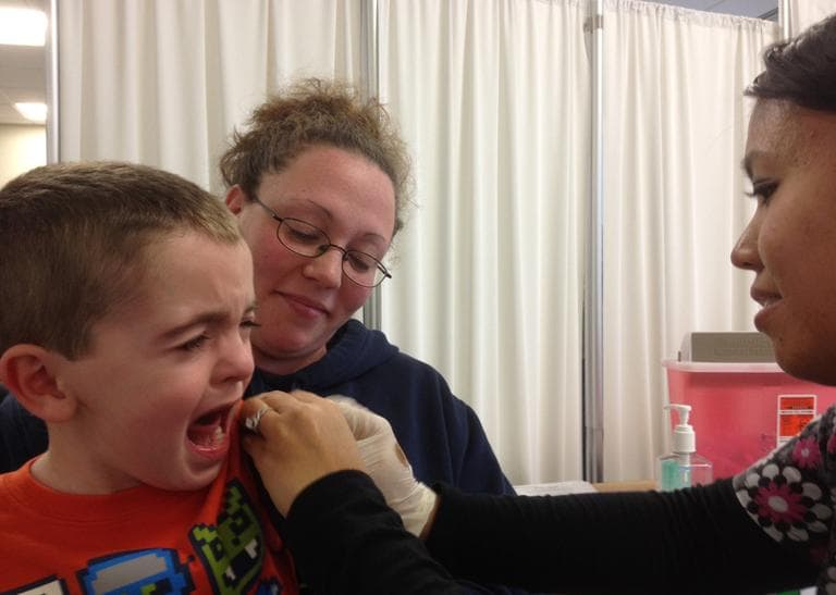 Lucas Rose is comforted by his mother, Julie Rose, after getting a flu shot from Vy Long at Harvard Vanguard in Quincy on Friday. (Martha Bebinger/WBUR)