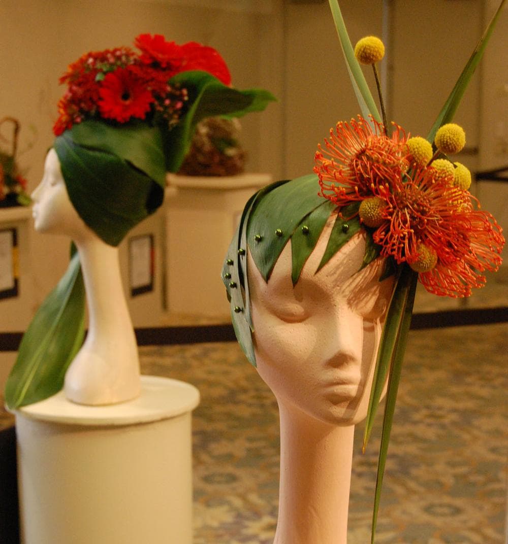 Joan Schofield of the Holliston Garden Club fashioned this hat out of flowers and palm leaves. A design by Cynthia Chace of the Community Garden Club of Cohasset and the Garden Club of Hingham is seen in the background. (Greg Cook)