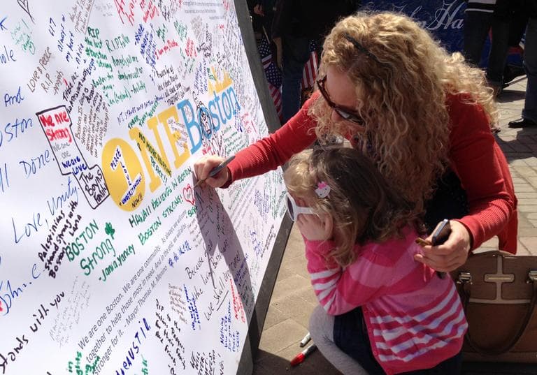 Heidi Barber and daughter Nadia write "Good night to Martin" on the memorial at Boylston Street Wednesday.  (Fred Bever/WBUR)
