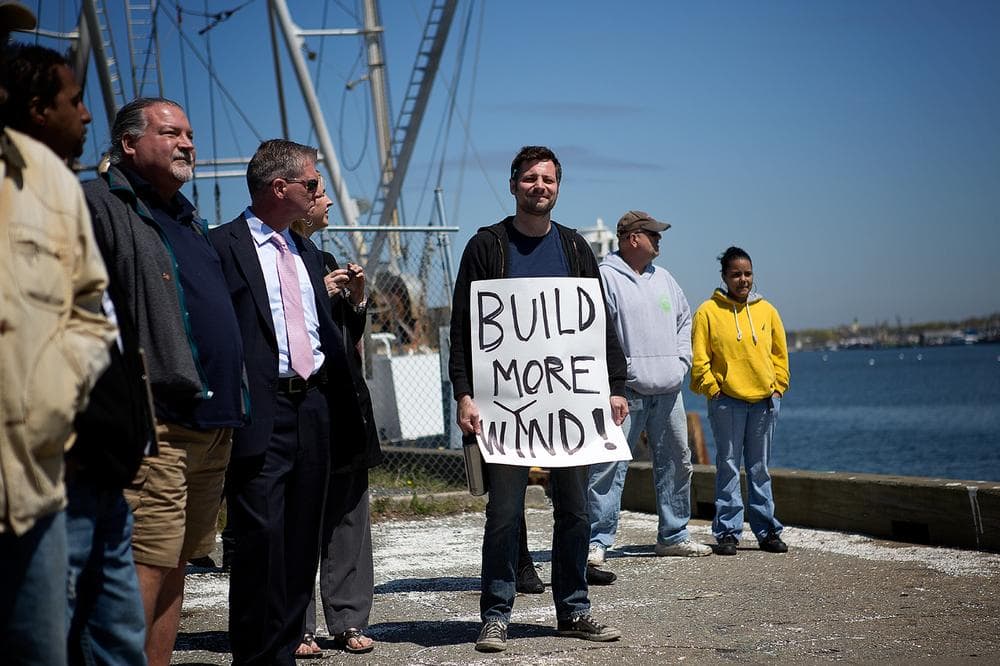 A man with a sign reading "Build more wind!" attends the ground-breaking ceremony for the New Bedford Marine Commerce Terminal. (Jesse Costa/WBUR)