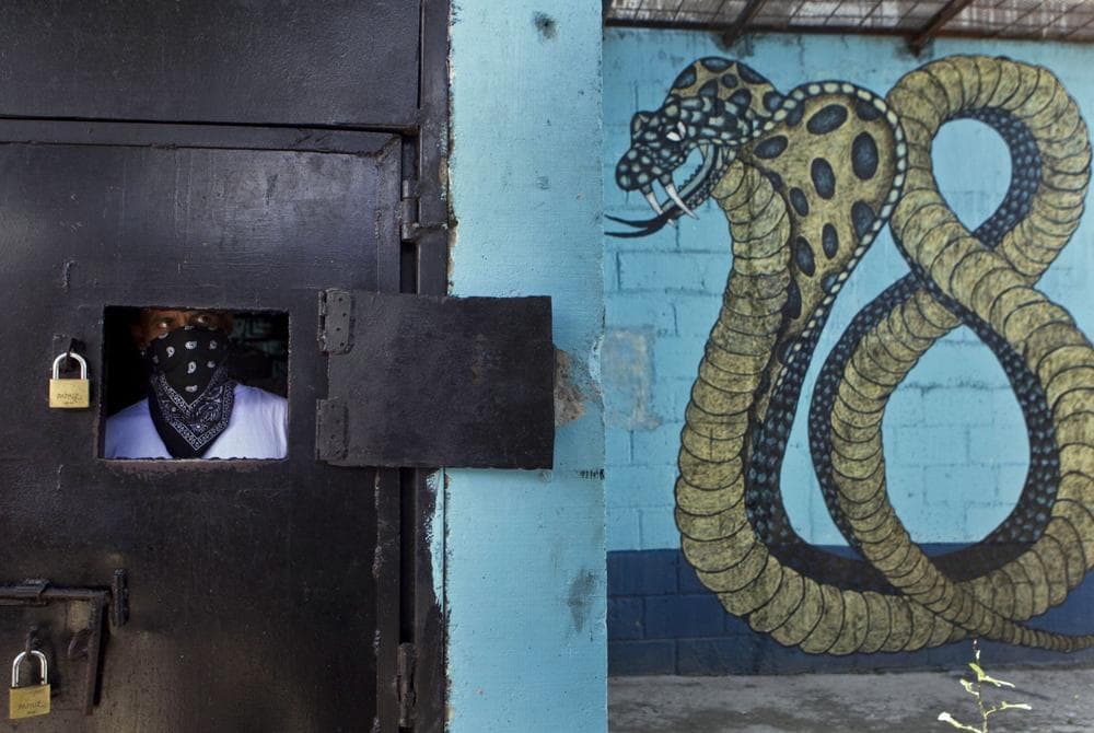 A masked member of the 18th Street gang peers from behind a window of a prison door as other gang members give a press conference inside the San Pedro Sula prison in Honduras, Tuesday, May 28, 2013. (Esteban Felix/AP)