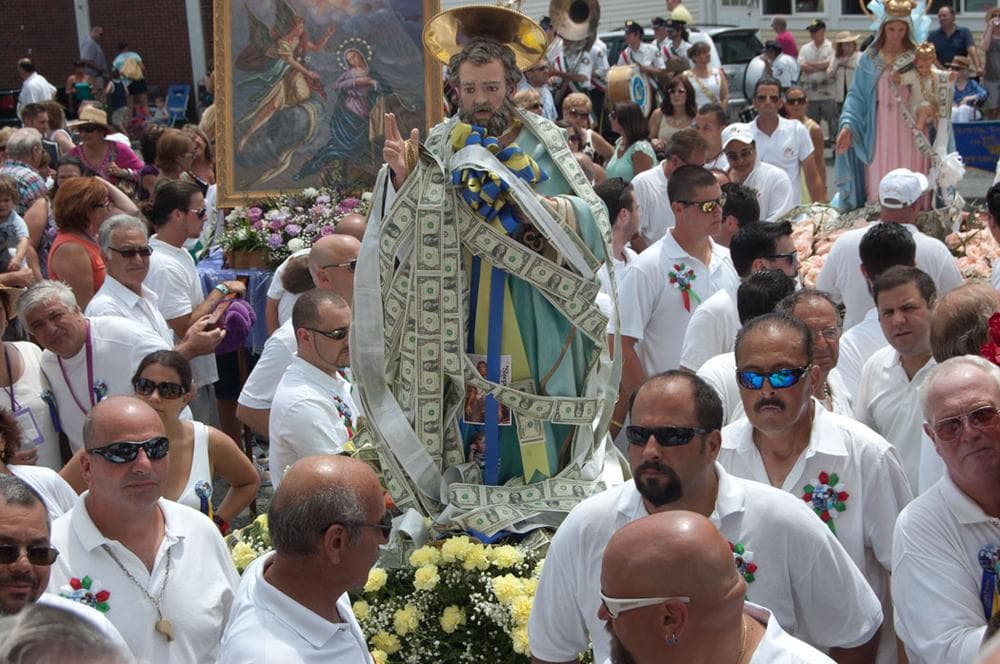 The St. Peter statue is wrapped in donations as Sunday’s procession pauses for prayer in front of Our Lady of Good Voyage Church. (Greg Cook)