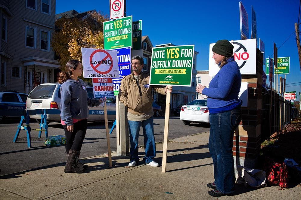 Sandra Najjar, Dino Tavano and Giordana Mecagni hold signs to either support or reject the casino plan for Suffolk Downs. (Jesse Costa/WBUR)
