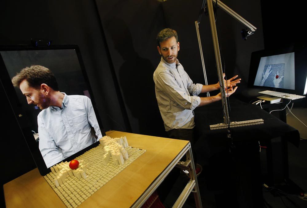 MIT graduate student Sean Follmer, a researcher with MIT's Tangible Media Group, moves his hands in front of a depth-sensing camera, which sends signals to a motorized pin screen, far left, where a 3D image pops up to manipulate the red ball. (Elise Amendola/AP)