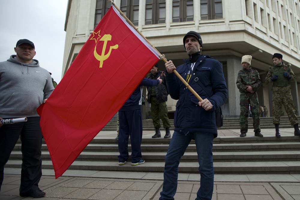 Local residents hold Sovivet flag as members of Cossack militia guard the local parliament building in Simferopol, Ukraine, on Thursday, March 6, 2014. Lawmakers in Crimea declared their intention Thursday to split from Ukraine and join Russia instead, and scheduled a referendum in 10 days for voters to decide the fate of the disputed peninsula. (AP)