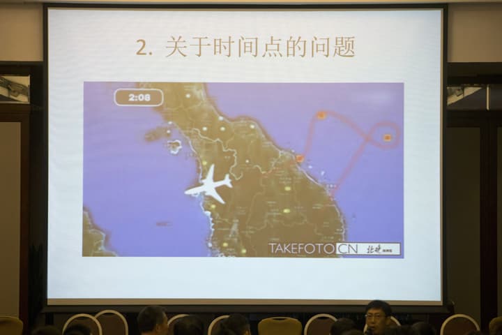 In this photo taken Saturday, March 22, 2014, a relative of Chinese passengers aboard the missing Malaysia Airlines, MH370, presents a slideshow showing a map of the route the missing plane took at a hotel meeting room in Beijing, China. The words on top reads "2. About the issue of time." (AP)