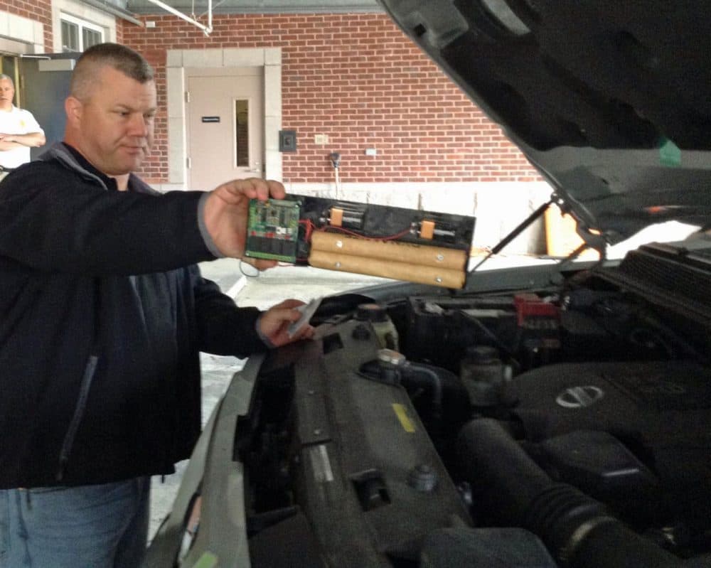 Master Sgt. Kenneth Huddleston, with the federal Department of Homeland Security’s mobile training unit, identifies a fake bomb under the hood of a car during a recent training session. (Deborah Becker/WBUR) 