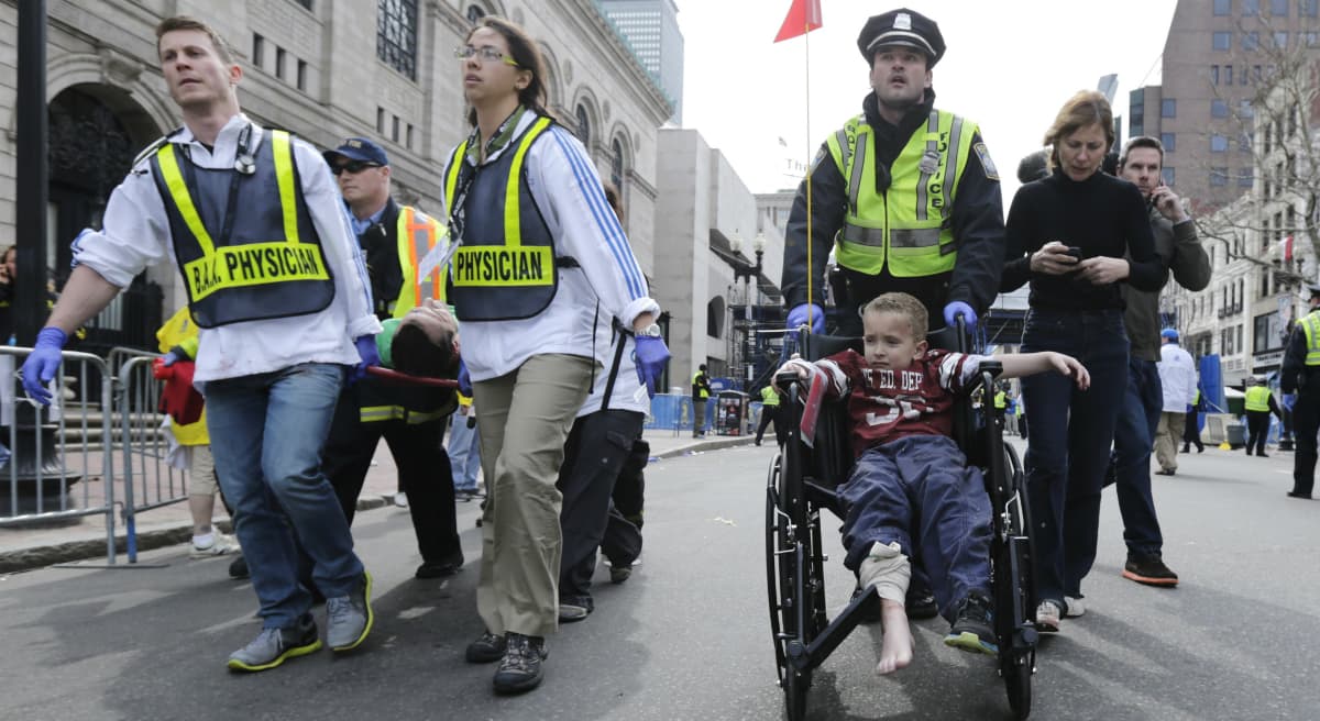 In this photo, a Boston police officer wheels in injured boy down Boylston Street as medical workers carry an injured runner following an explosion during the 2013 Boston Marathon in Boston, Monday, April 15, 2013. (Charles Krupa/AP) 