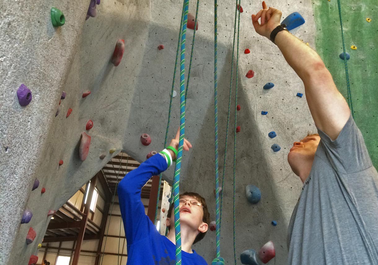 A volunteer shows a child how to rock climb at an event in Watertown. (Fred Thys/WBUR)