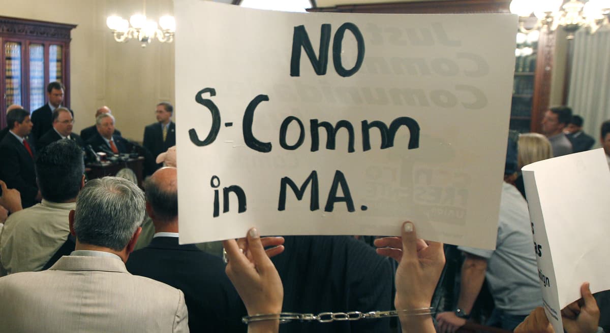 In this file photo, protesters wearing handcuffs holds up signs urging the stop of the "Secure Communities" program, or "S Comm," at a news conference held by Massachusetts county sheriffs at the Statehouse in Boston, Wednesday, Sept. 28, 2011. (Charles Krupa/AP)