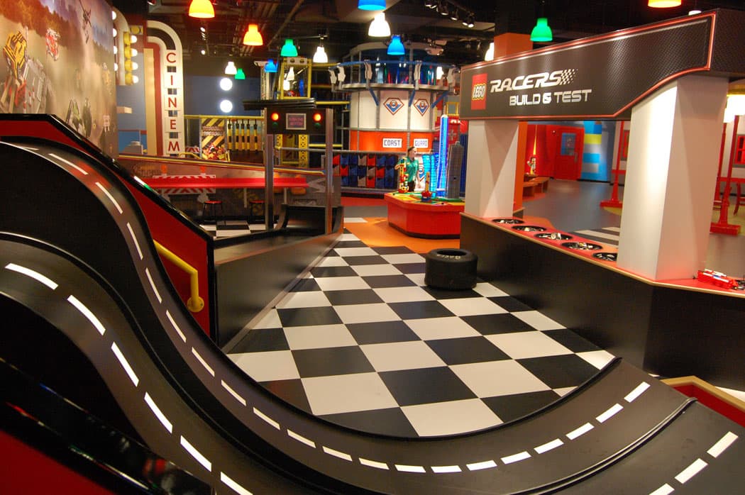 The “Lego Racers: build and Test” area offers tracks to roll custom Lego built vehicles down. In the left background is the “Lego 4D Cinema.” The Coast Guard cutter and “Fire Academy” in the middle background offer a climbing maze and slide as well as large rubber Lego blocks to play with. (Greg Cook).
