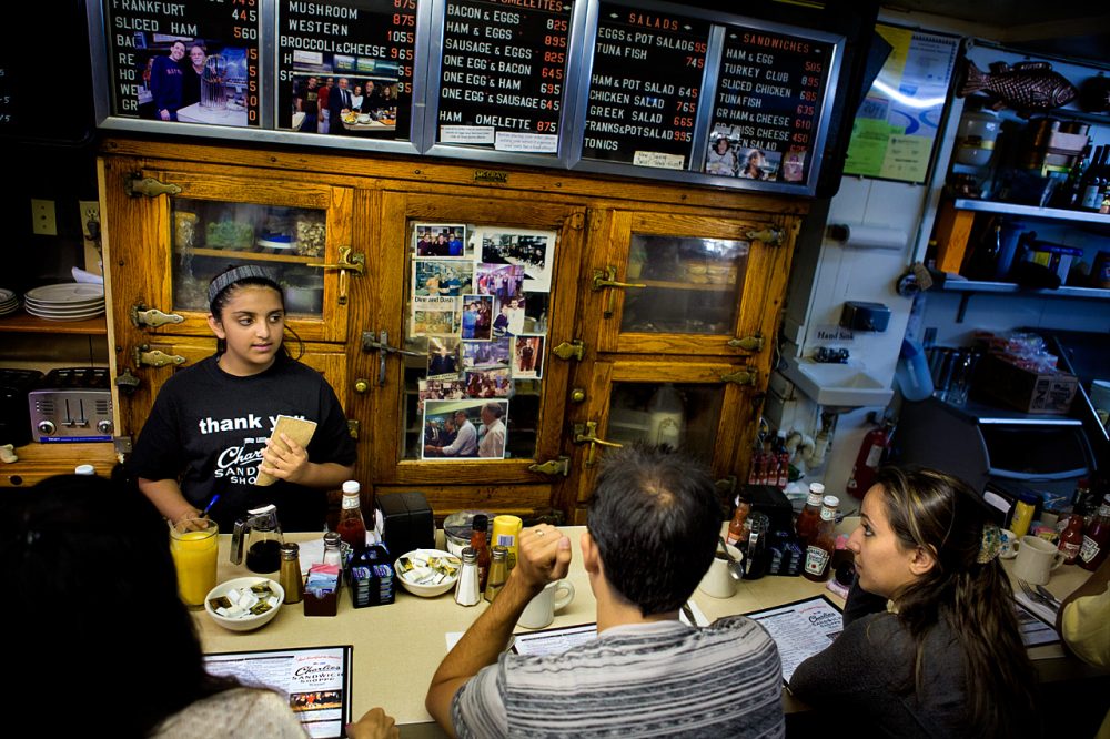 A waitress taking and order at the counter in front of the old wooden refrigerator with photos of celebrities that have visited the restaurant including President Obama. (Jesse Costa/WBUR).