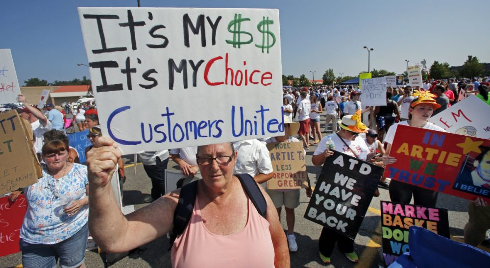 Why community, state and regional leaders have an enormous stake in resolving the Market Basket fiasco. Pictured: Protesters hold signs during a rally at Market Basket in Tewksbury, Mass., Tuesday, Aug. 5, 2014. Thousands of Market Basket supermarket employees and their supporters are calling for the reinstatement of their fired CEO, even as the company began a three-day job fair to replace employees who have refused to work during a revolt that is costing the supermarket chain millions. (Elise Amendola/AP)