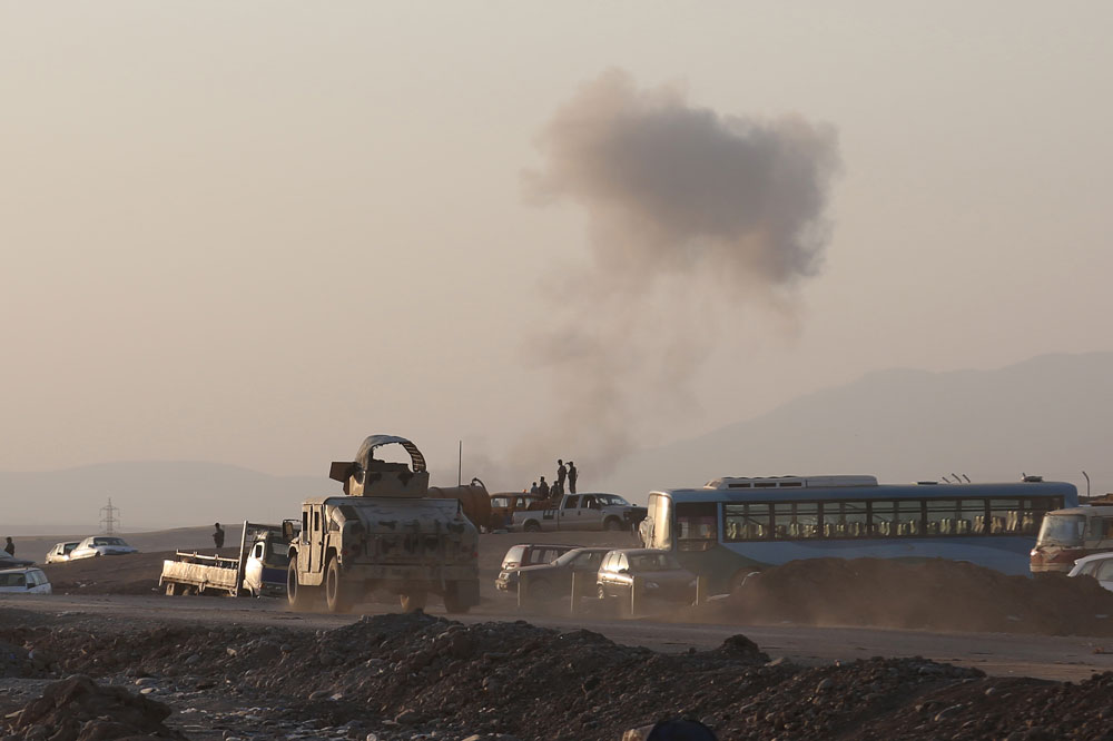 An armored vehicle belonging to Kurdish Peshmerga fighters rushes to a bombing site as smoke rises after airstrikes targeting Islamic State militants near the Khazer checkpoint outside of the city of Irbil in northern Iraq, Friday, Aug. 8, 2014. (AP/ Khalid Mohammed)