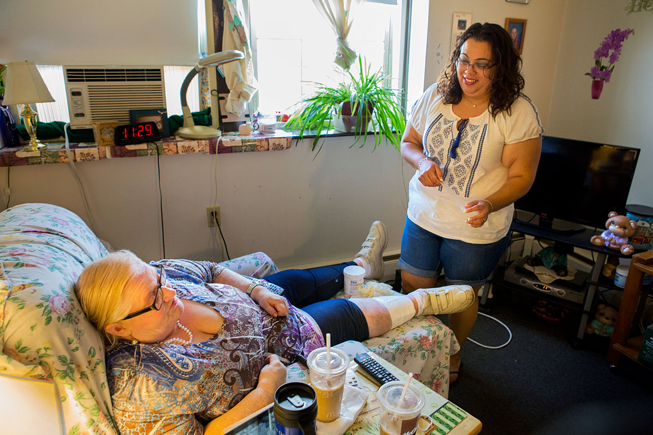 Rosario Cabrera, right, attends to Donna, her "consumer," in Donna's New Bedford living room. The personal care attendant makes $13.88 an hour, but hopes for benefits like sick time. (Jesse Costa/WBUR)