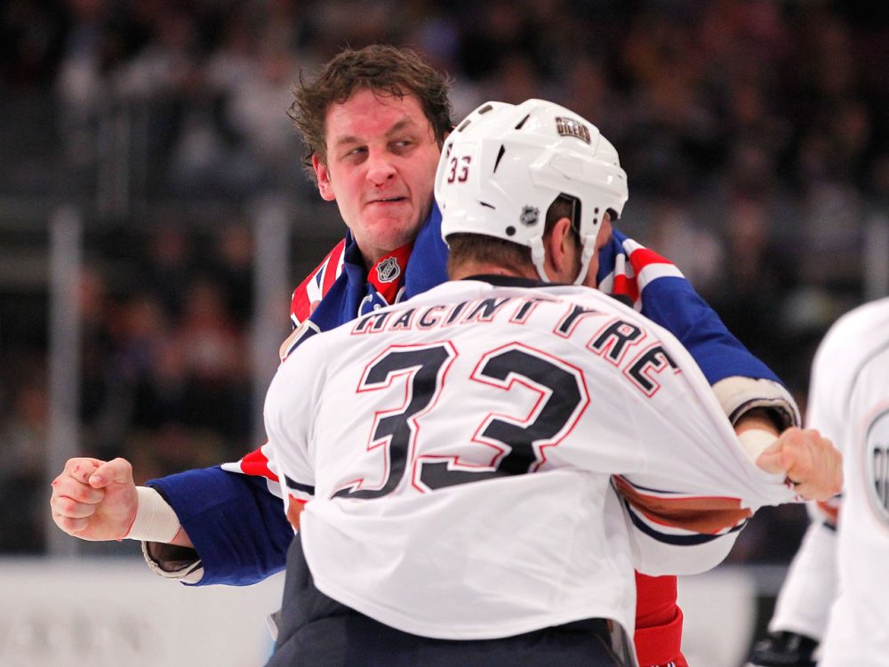 Derek Boogaard (in blue) played the role of hockey enforcer -- and by his own estimate may have suffered hundreds of concussions. (Paul Bereswill/Getty Images)