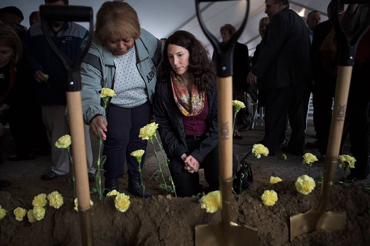 Myrnairis Cepeda, left, sets a yellow carnation into the ground in honor of her daughter who was killed in a car accident in the U.S. after several tours of duty overseas. Maggie Brothers, right, is an Army Survivor Outreach Services Support Coordinator for Massachusetts whose husband died from exposure to radiation in Qatar. (Jesse Costa/WBUR)