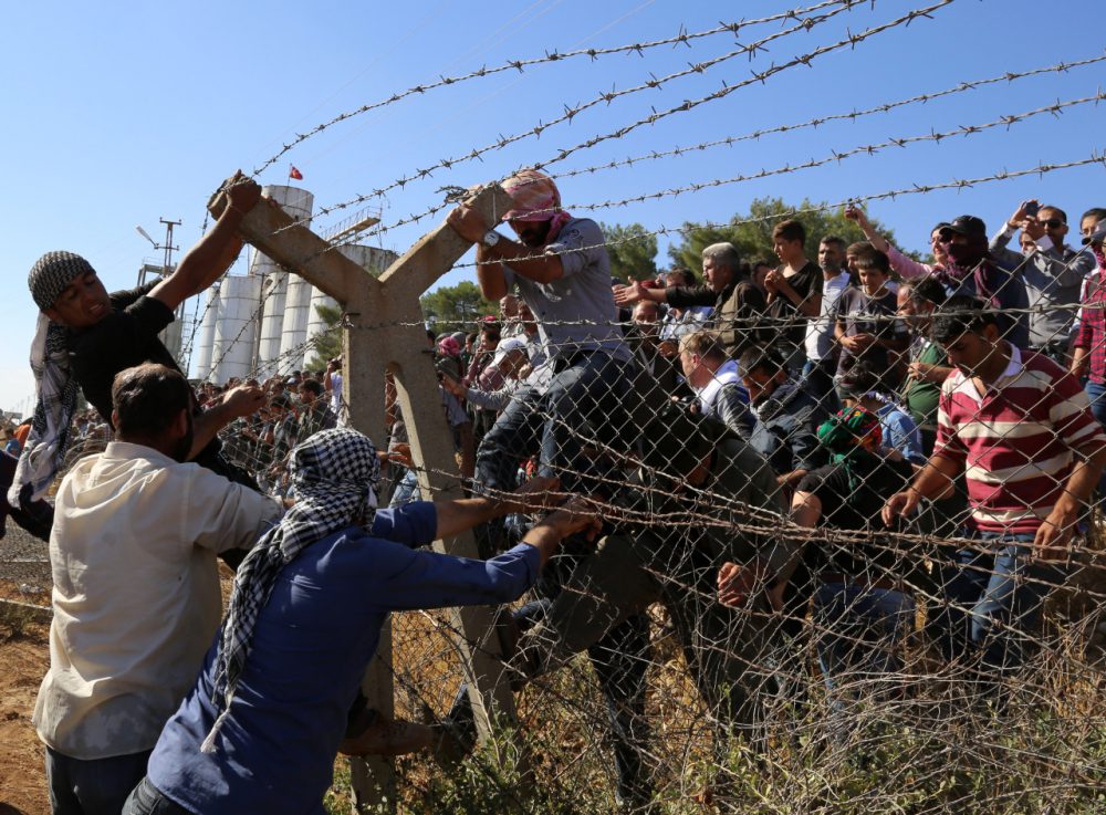 In this Friday, Sept. 26, 2014 photo, Kurds from Turkey, right, and Syria break down the barbed wire at the Turkey-Syria border near Suruc, Turkey. Turkish President Recep Tayyip Erdogan said Friday that a &quot;no-fly zone&quot; should be created in Syria to protect part of it from attacks by Syria's air force. In his comments to reporters on his return from the U.N. General Assembly in New York, Erdogan did not specify where such a zone should be located. (AP)