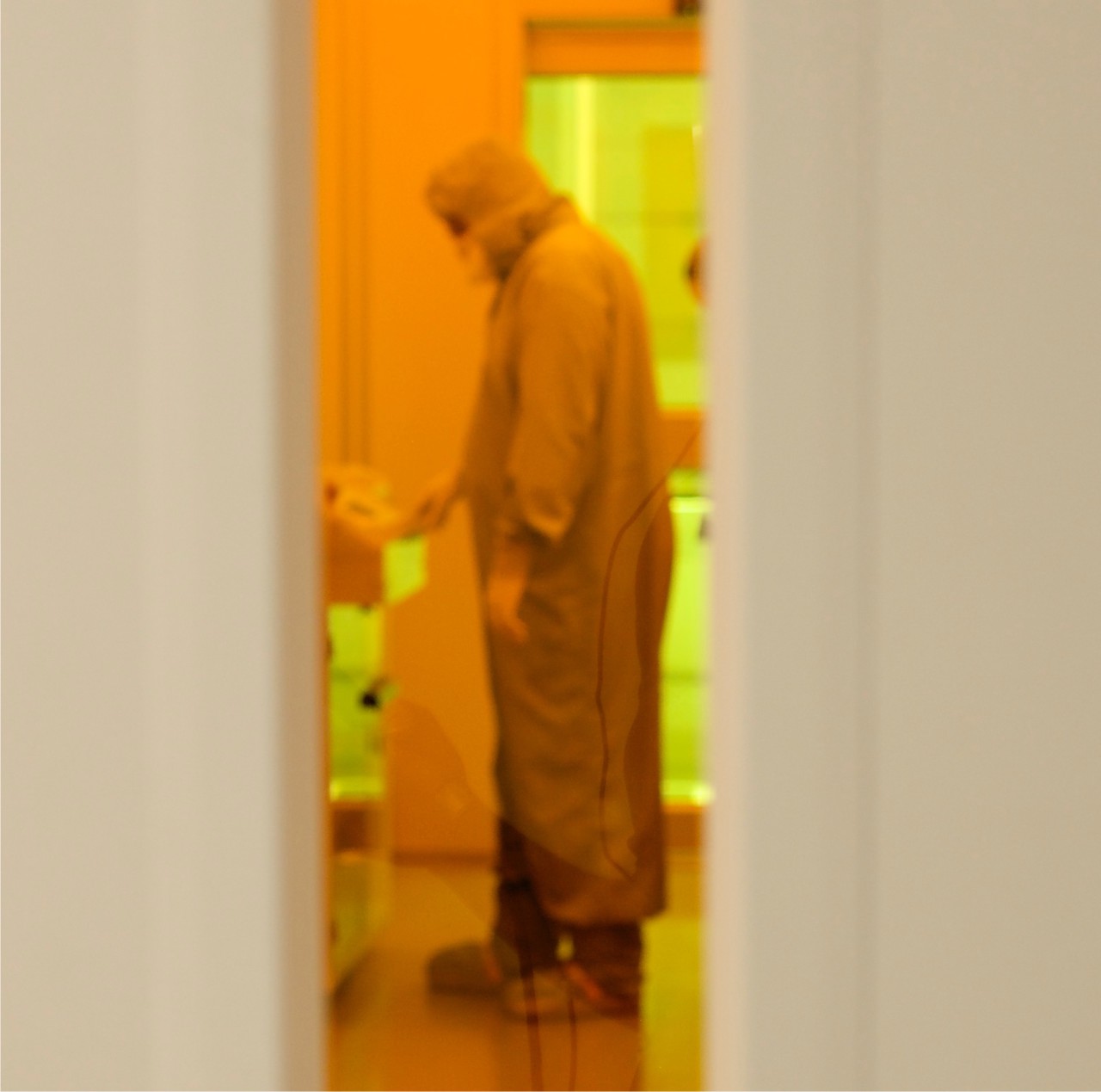 A Draper Laboratory worker behind the glass of a clean room in the microfabrication lab. (Photo: Katherine Gorman, WBUR)