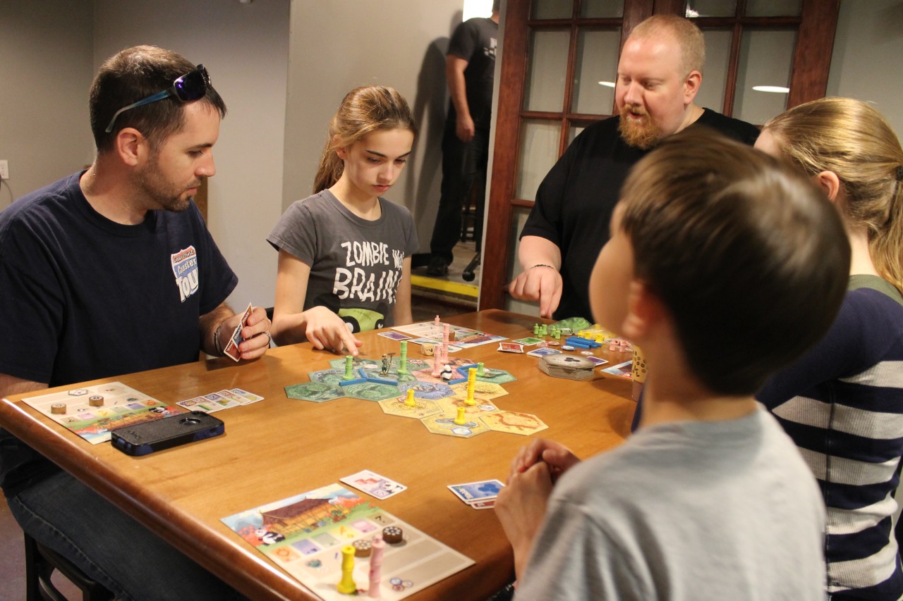 A volunteer at Spielbound explains the rules of Takenoko, an obscure Japanese board game, to the Short family. (Robyn Murray/OAG)