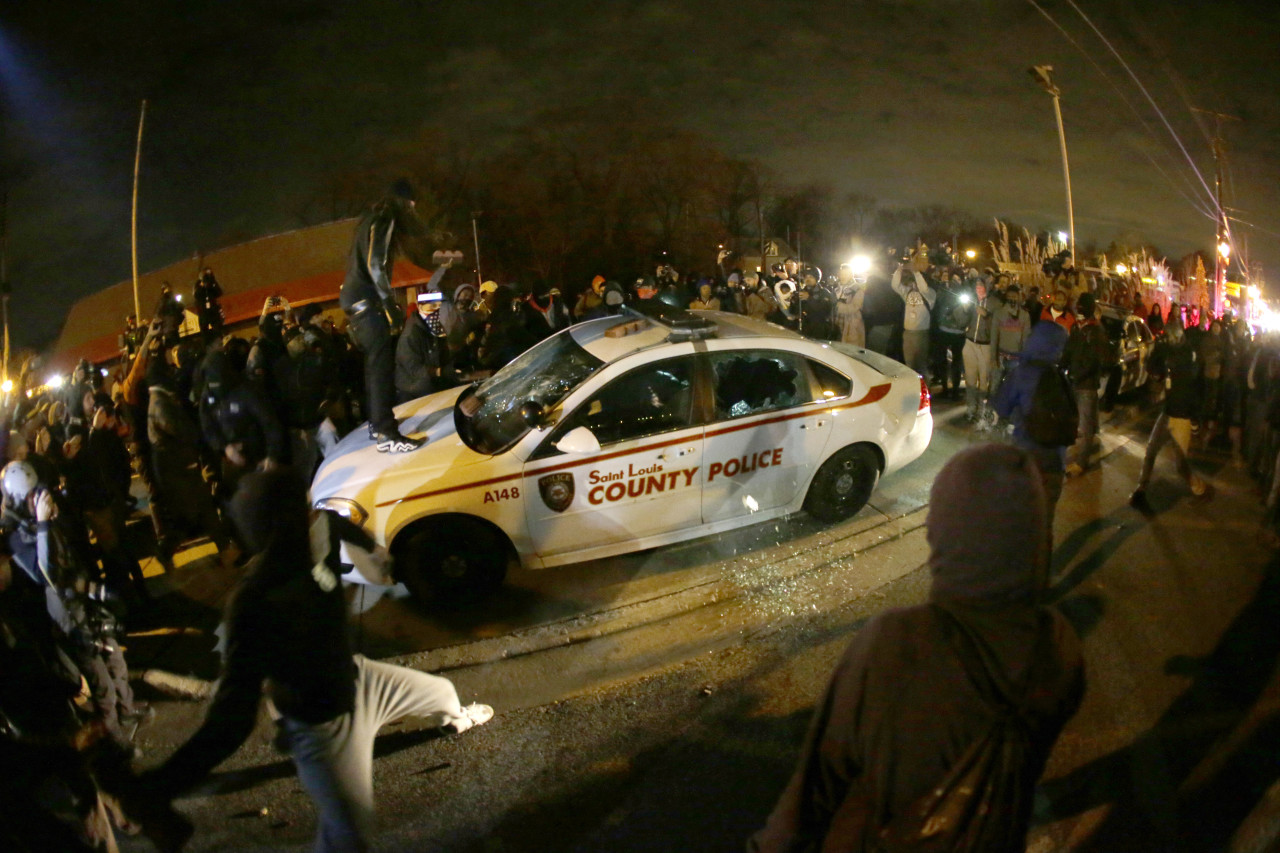 A protester squirts lighter fluid on a police car as the car windows are shuttered near the Ferguson Police Department. (Charlie Riedel/AP)