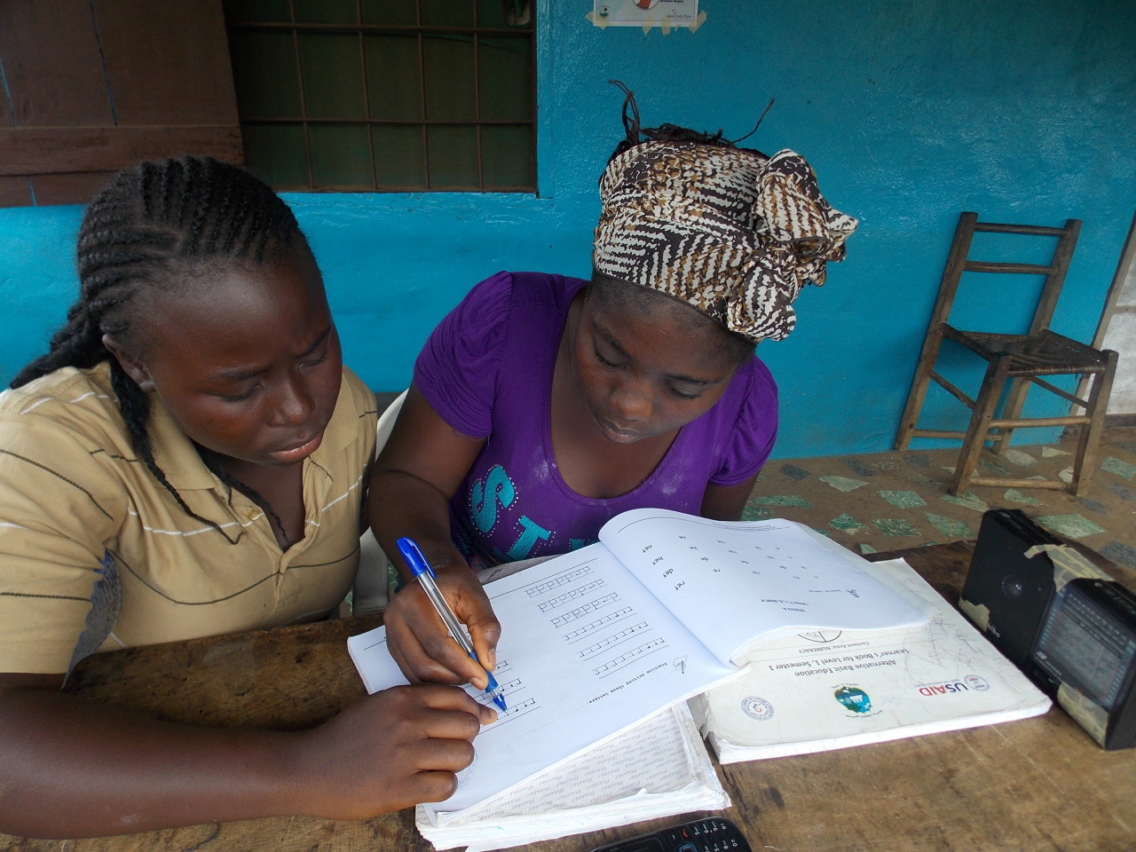 In Montserrado, Liberia, Vivian Dennis, right, works with her “study buddy,” Henrietta Sherman, in workbooks provided by the EDC-USAID education program now being broadcast on 10 community radio stations while schools are shut down due to Ebola. Her radio is to the right. (Courtesy EDC)