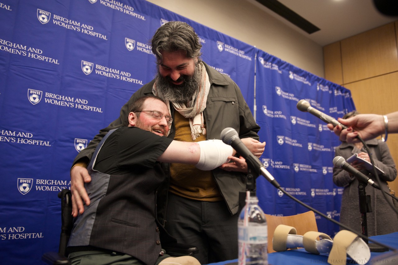 Arm transplant recipient Will Lautzenheiser uses his new arms to hug his partner, Angel Gonzalez, at a Brigham and Women's Hospital press conference. (Photo courtesy BWH)