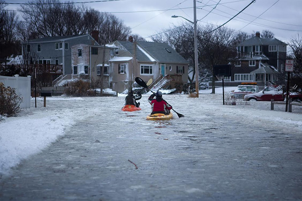Kayakers head down a flooded Otis Road in Scituate. The first storm of 2014 also dropped 2 feet of snow on parts of the state. (Jesse Costa/WBUR)