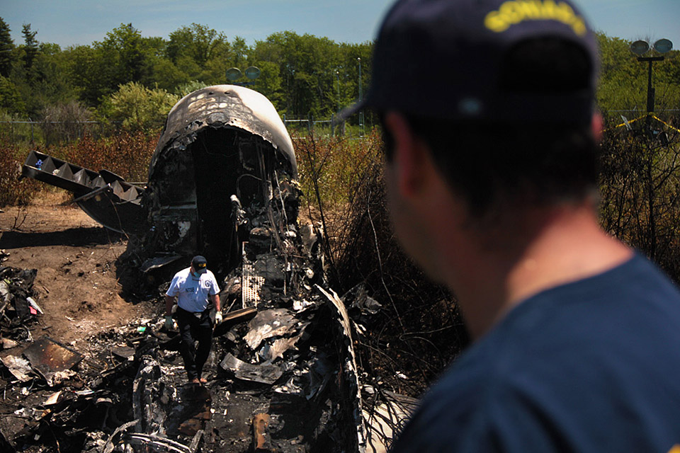 Wreckage lay at the scene in Bedford, where a private plane plunged down an embankment and erupted in flames during a takeoff attempt at Hanscom Field on May 31. Seven people died in the crash. (Fred Thys/WBUR)