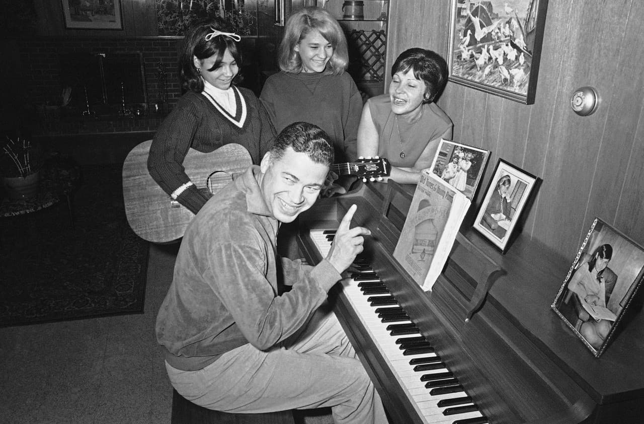 Then Massachusetts, Attorney General Edward W. Brooke plays piano as he joins his family in an afternoon of relaxation in their Newton, Massachusetts, home, Jan. 15, 1966. Joining in the fun are from left, daughters Edwina, 13, and Remi, 16, and Mrs. Brooke.
