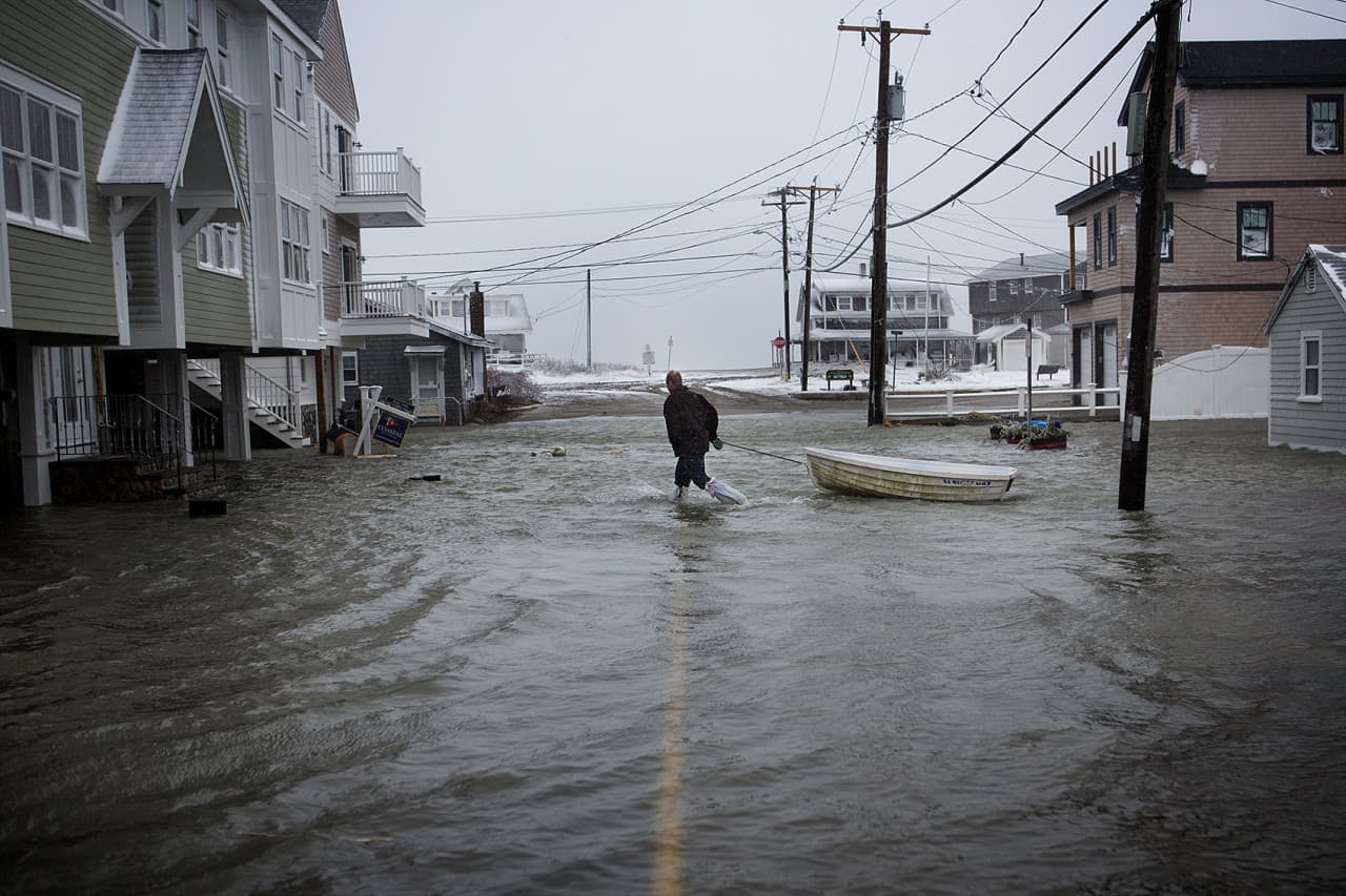 A man wearing trash bags on his feet tows a dingy in Scituate. (Jesse Costa/WBUR)