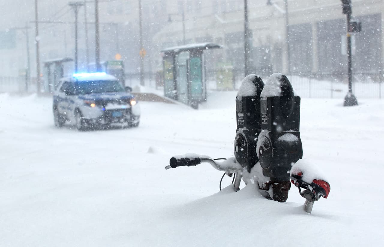 A police vehicle hurries down Commonwealth Avenue, past a bicycle and parking meter almost buried in snow. (Robin Lubbock/WBUR)