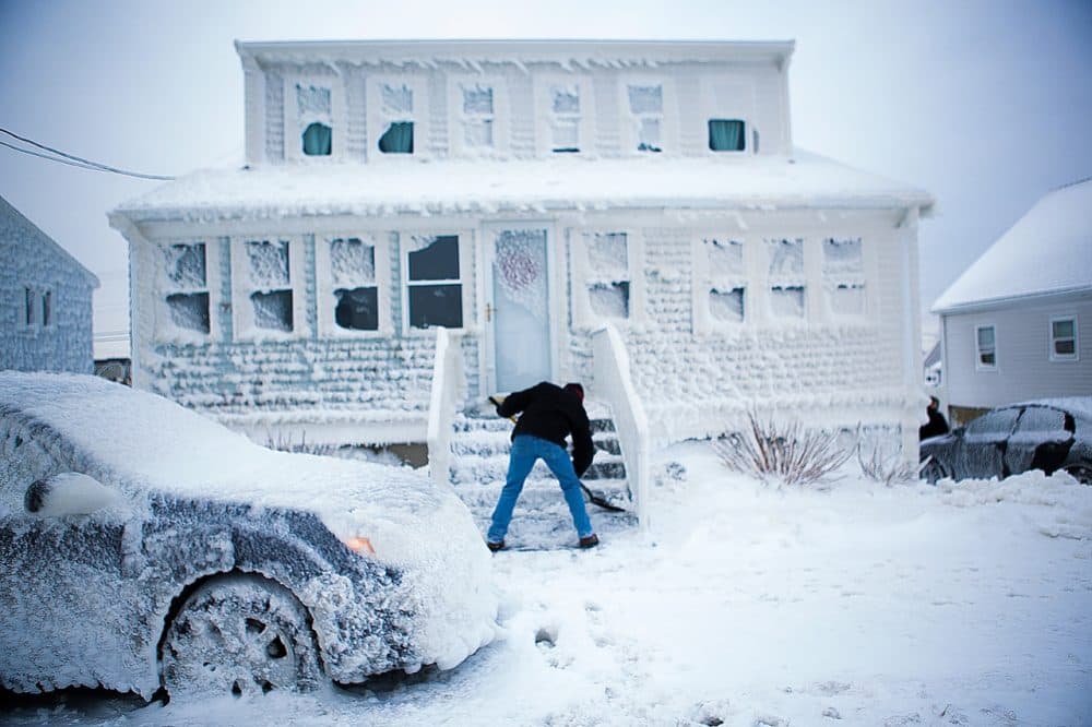 Paul Rugg digs out of his sea-sprayed house on Foster Street in the Brandt Rock area of Marshfield. He had to climb out the window in order to open the front door. (Jesse Costa/WBUR)