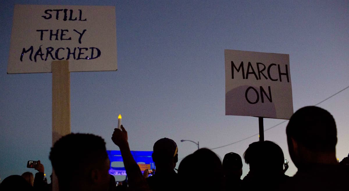 Carol Rose: It’s time for us to act on the protests in Boston and across America with concrete policy reforms to restore community faith and trust in those who pledge to protect and serve us all, equally. In this photo, marchers hold up signs as they make their way towards the Edmund Pettus Bridge in honor of Martin Luther King Jr., Sunday, Jan. 18, 2015, in Selma, Ala. (Brynn Anderson/AP)