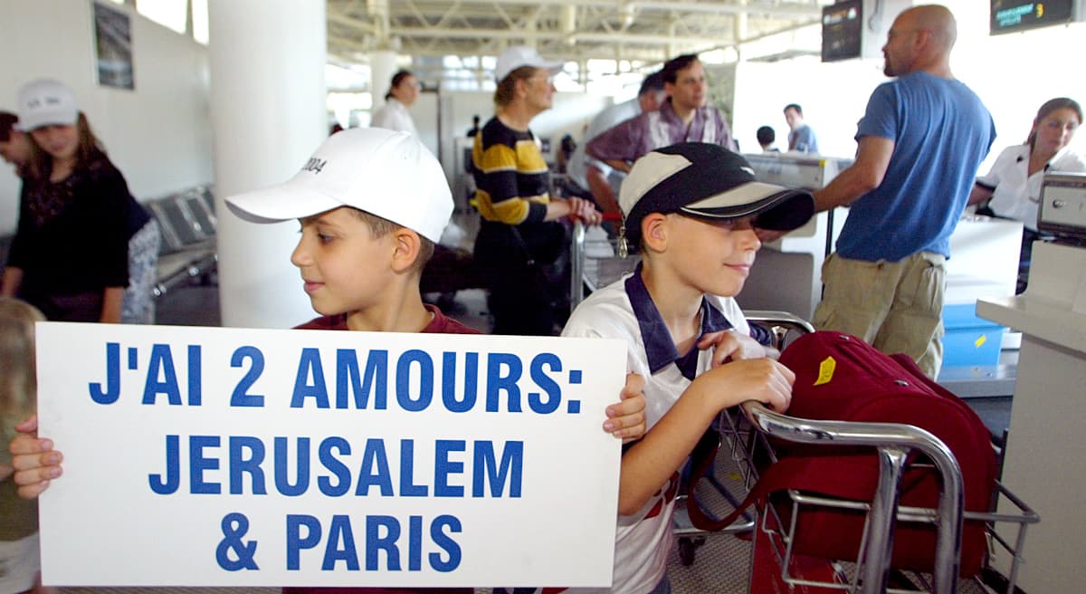 A boy holds a placard that reads, "I have two loves, Jerusalem and Paris," as his family checks in at Charles de Gaulle airport in Roissy, north of Paris, before boarding a plane bound for Tel Aviv, Israel, along with about 200 other emigrating French Jews, in July, 2004. The number of Jews leaving France for Israel has risen steadily over the past decade. (Franck Prevel/AP)