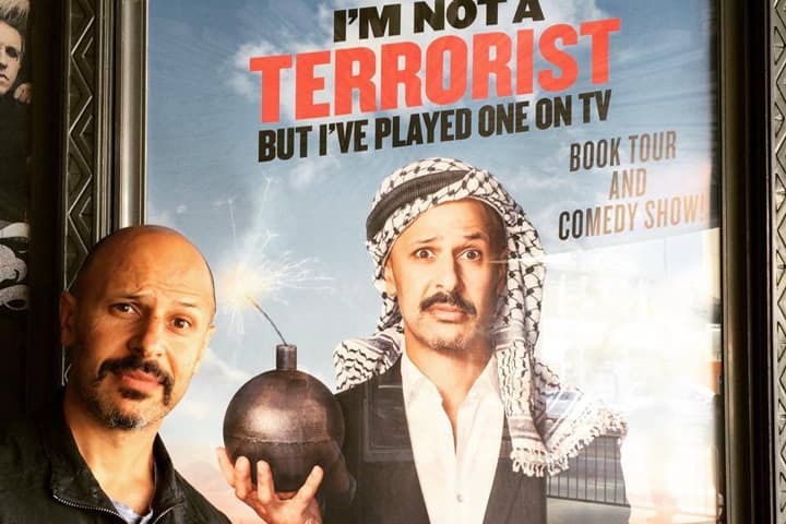Comedian and author Maz Jobrani stands next to a promotional photo for his ongoing book tour in Los Angeles, CA. (Courtesy Maz Jobrani)
